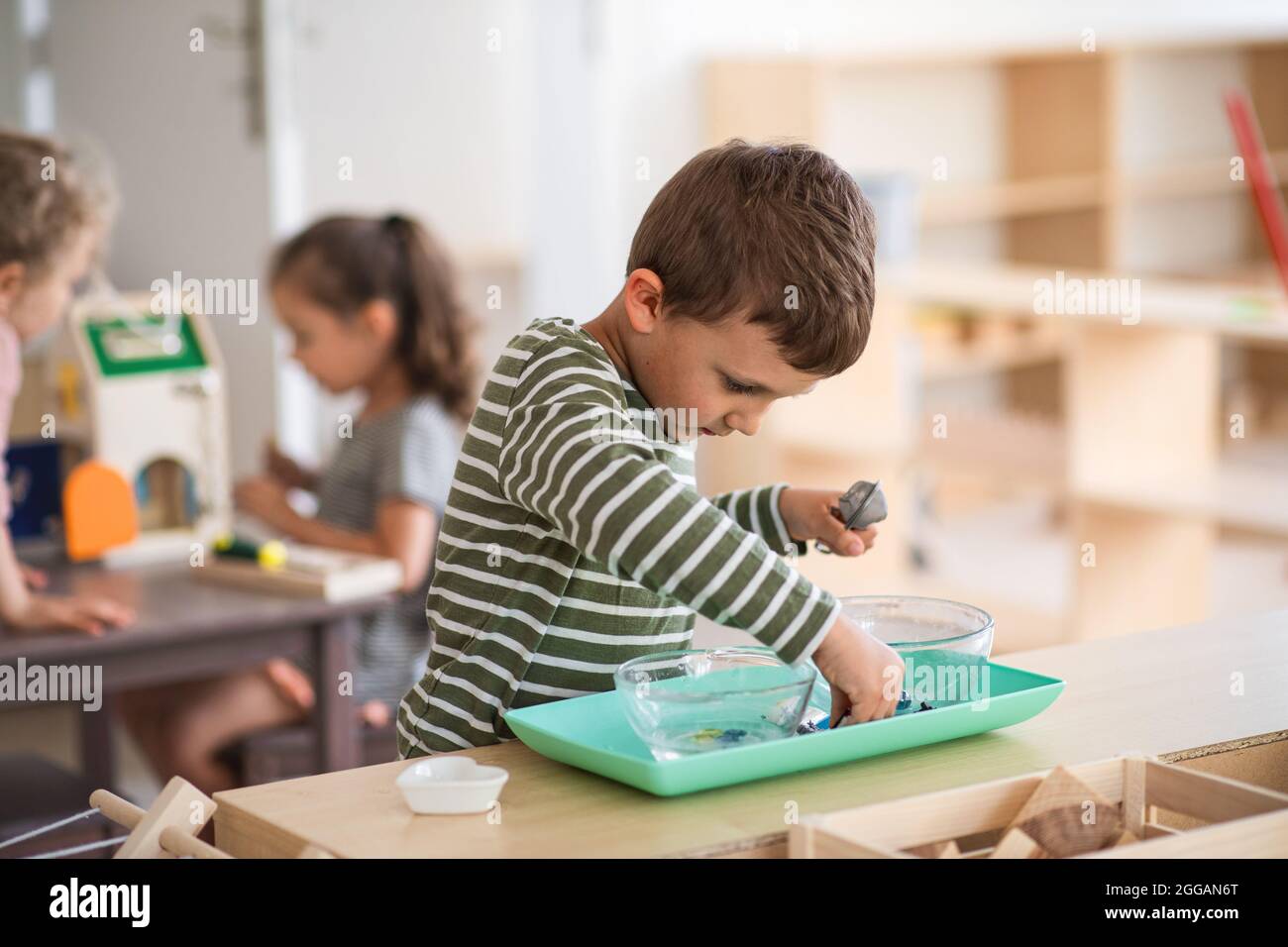 Kleiner Kindergarten Junge spielt drinnen im Klassenzimmer, montessori lernen. Stockfoto