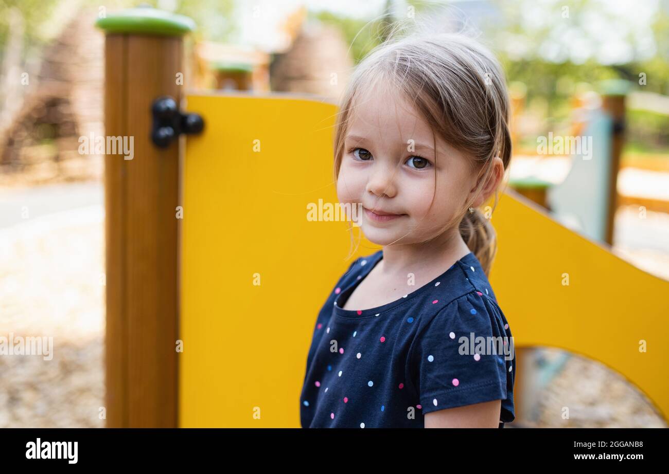Kleines Mädchen aus dem Kindergarten, das draußen auf dem Spielplatz steht und die Kamera anschaut. Stockfoto