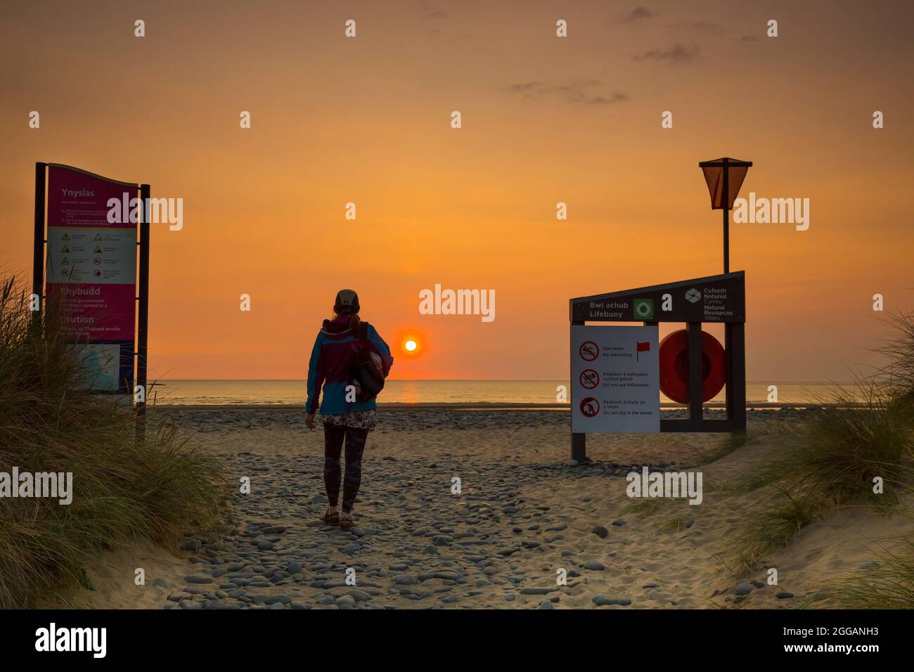 Rückansicht einer isolierten jungen Frau, die am Strand bei Sonnenuntergang an einem britischen Strand spazieren ging, während des Sommerurlaubs. Stockfoto