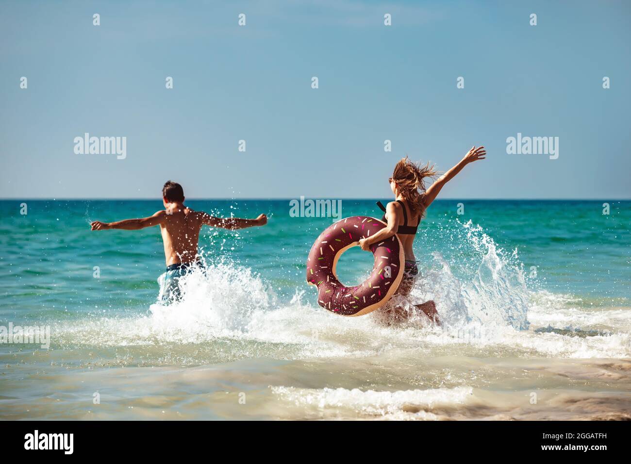 Glückliches junges Paar hat Spaß mit aufblasbarem Donut am Strand. Tropisches Urlaubskonzept Stockfoto