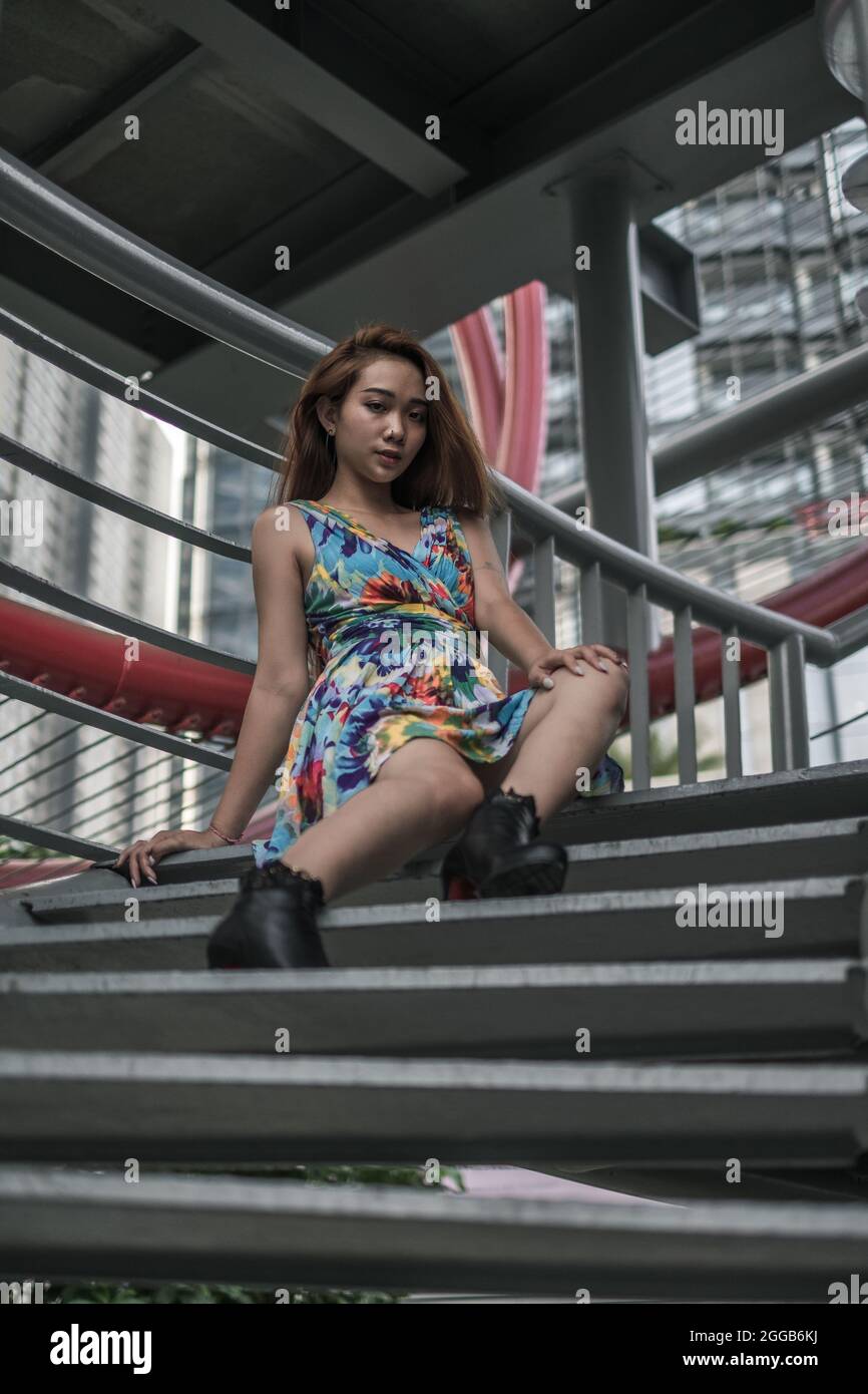 Schöne asiatische junge Frau in lässigen bunten Kleid sitzt im Freien. Langes Haar. Schöne Haltung. Hochwertige Fotos Stockfoto