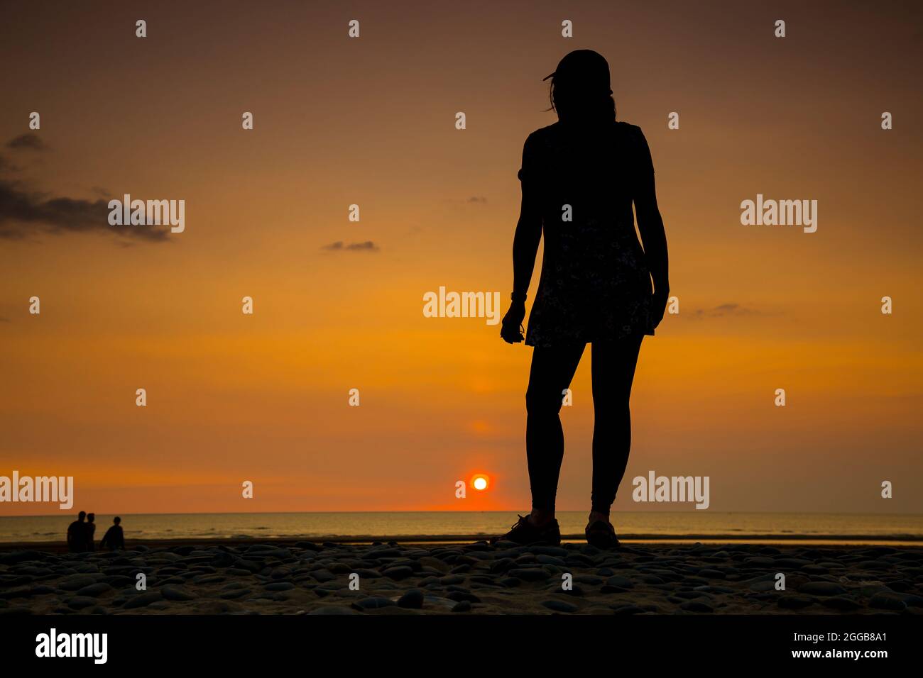 Rückansicht Silhouette einer isolierten jungen Frau, in Sportmütze, Blick auf das Meer bei Sonnenuntergang auf einem britischen Strand, Aufenthalt Sommerurlaub. Stockfoto