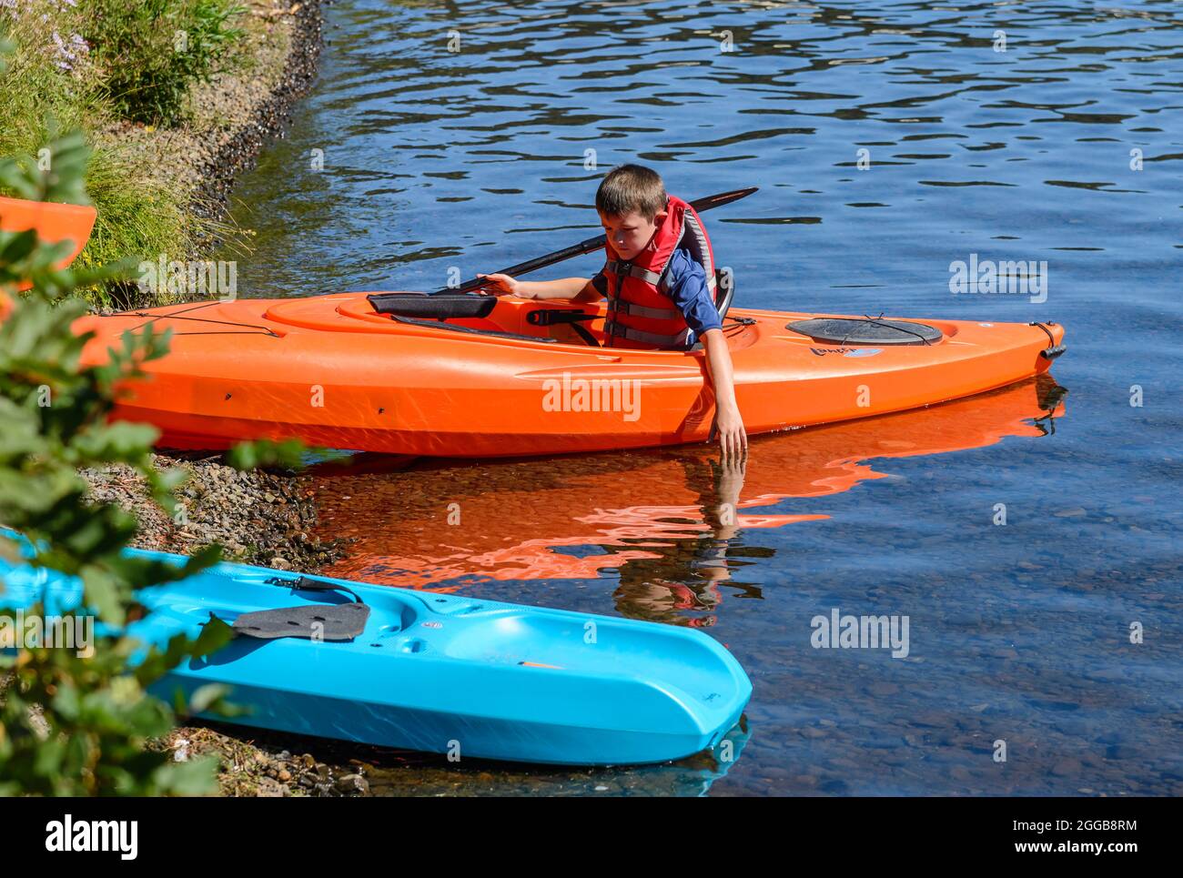 Ein kleiner Junge versucht, ein Kanu in einen See zu starten. Oregon, USA. Stockfoto