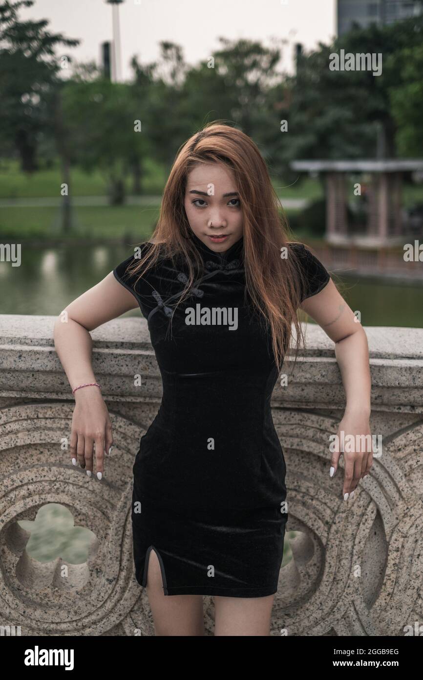 Schöne junge asiatische Frau in lässigen schwarzen Kleid in der Nähe von Handlauf im Park stehen. Langes Haar. Schöne Haltung. Reizende Vietnamesin. Stockfoto