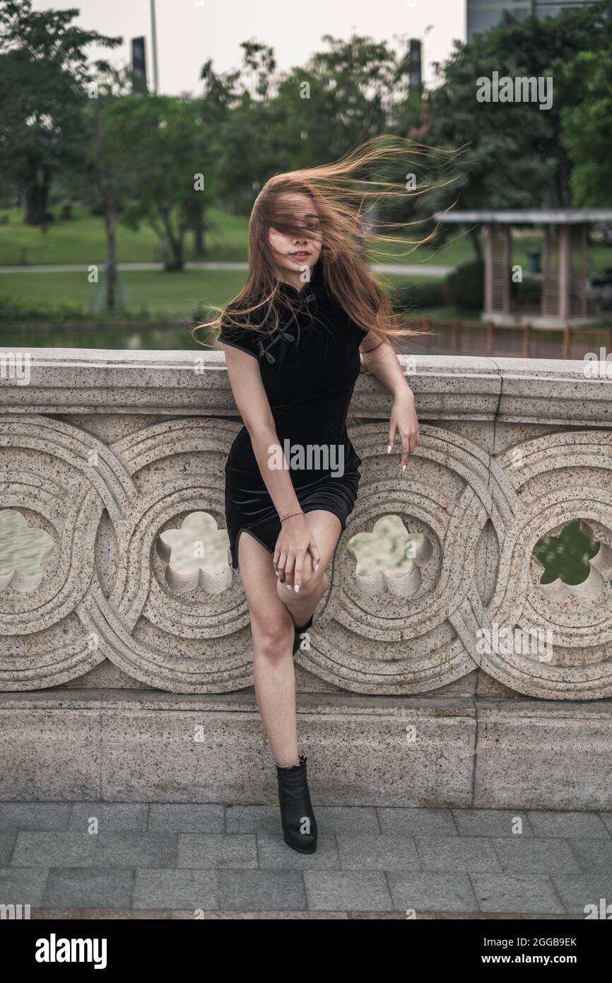 Schöne junge asiatische Frau in lässigen schwarzen Kleid in der Nähe von Handlauf im Park stehen. Wind in ihren Haaren. Schöne Haltung. Reizende Vietnamesin. Stockfoto
