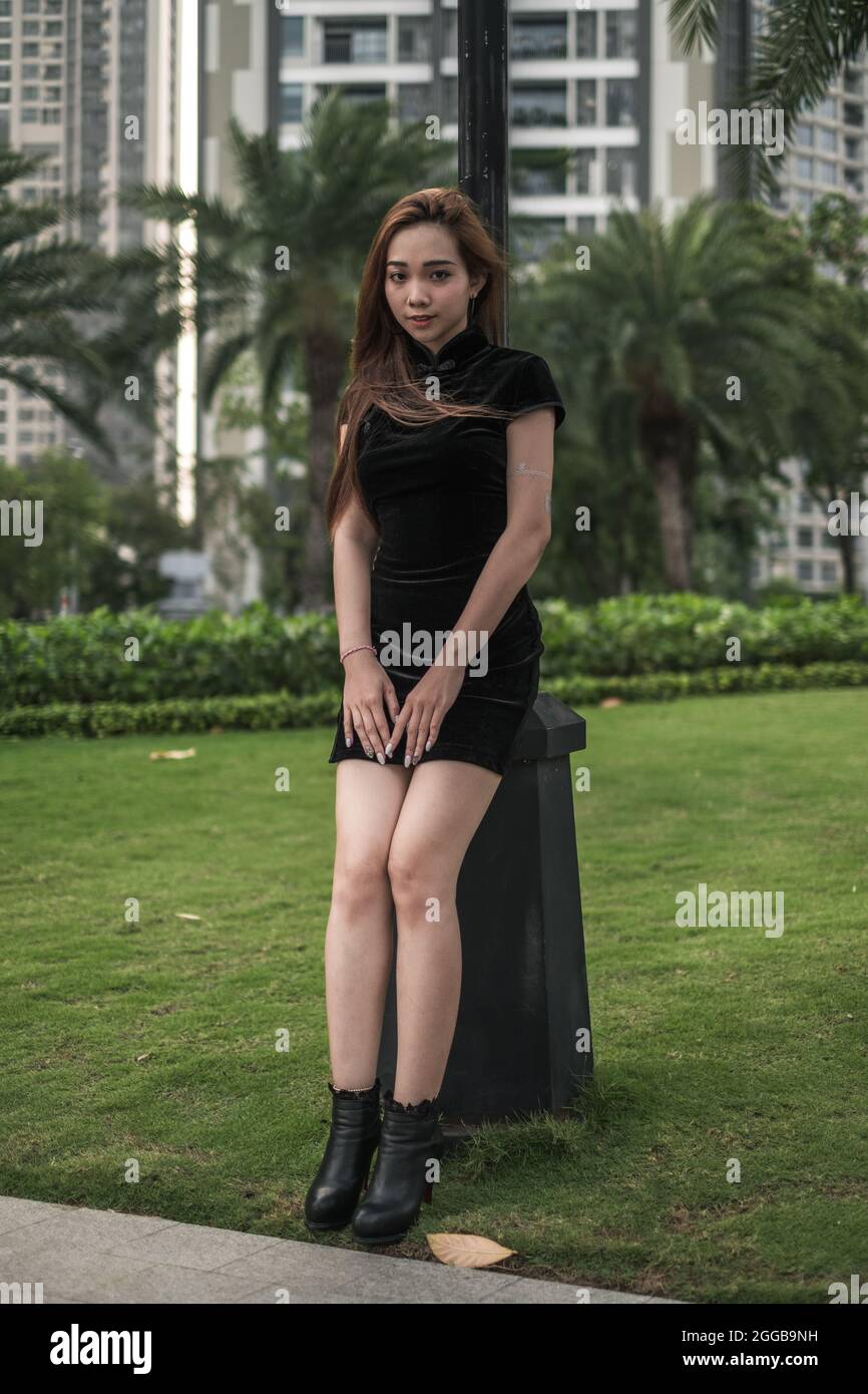 Schöne junge asiatische Frau in lässigen schwarzen Kleid auf der Straße mit Palmen stehen. Langes Haar. Schöne Haltung. Reizende Vietnamesin. Stockfoto