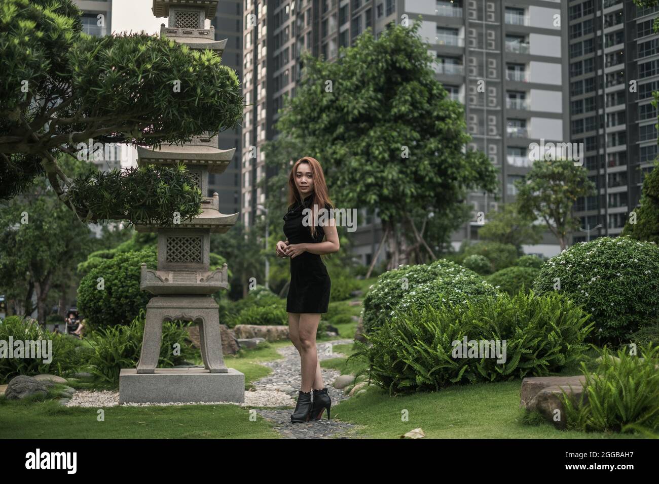 Schöne schlanke junge asiatische Frau in schwarzem Minikleid zu Fuß im Park. Langes Haar. Schöne Haltung. Seitenansicht. Bild von der Seite. Stockfoto