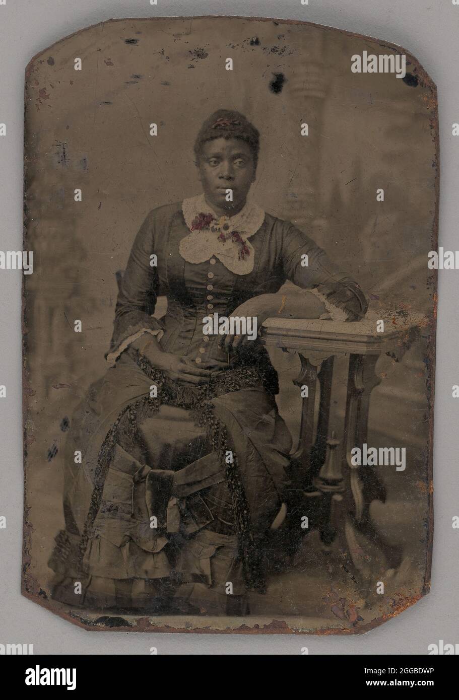 Ohne Titel (Porträt einer sitzenden Frau), 1880. Schwarz-weiß-Porträt einer dunkelhäutigen Frau, die vor einem bemalten Hintergrund in einem Kleid mit Spitzenkragen sitzt und den linken Arm auf einem kleinen Tisch ruht. Stockfoto