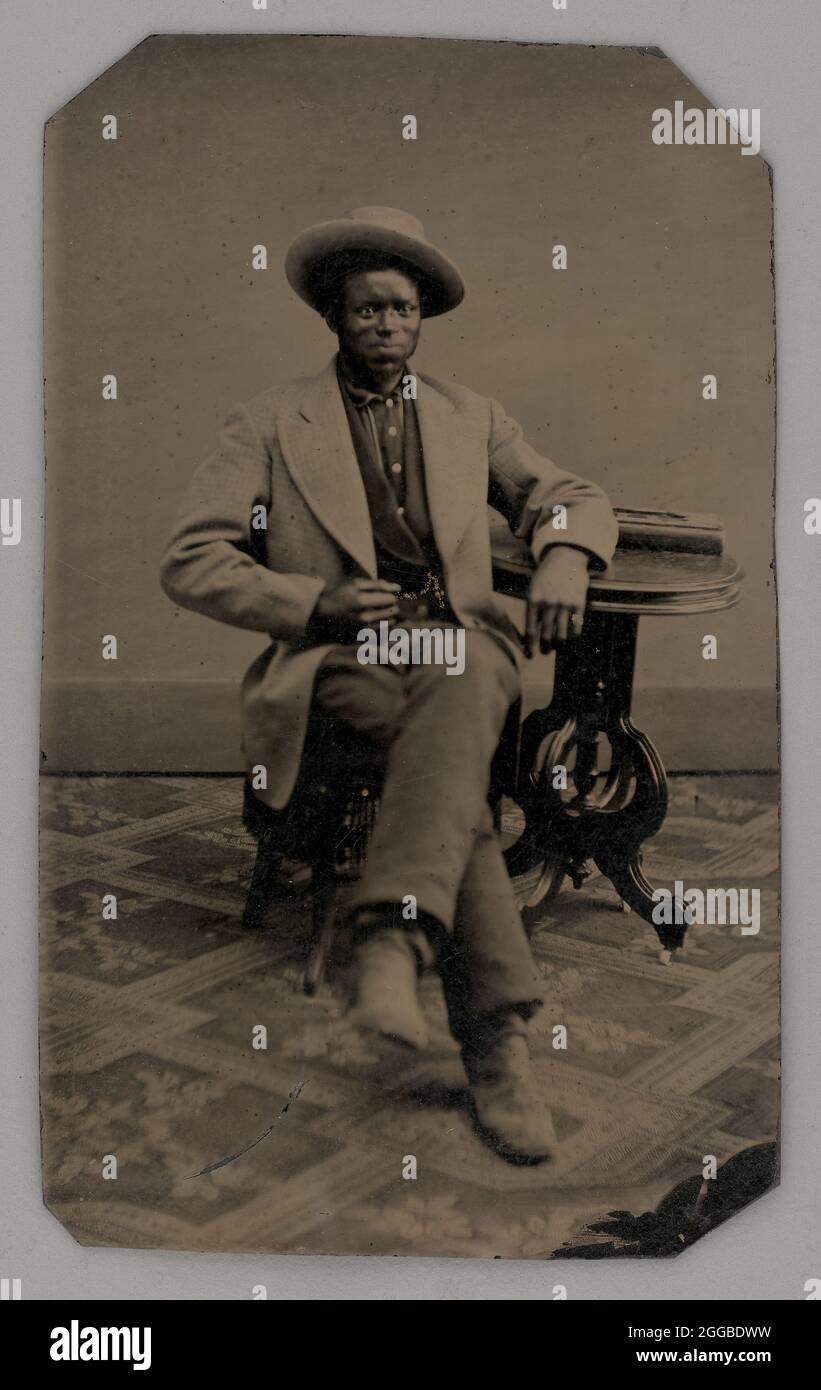 Ohne Titel (Portrait of a Seated man), 1880. Schwarz-Weiß-Porträtfoto eines dunkelhäutigen Mannes in einer hellen Jacke auf einem gemusterten Teppich, linker Arm auf einem kleinen Tisch. Stockfoto