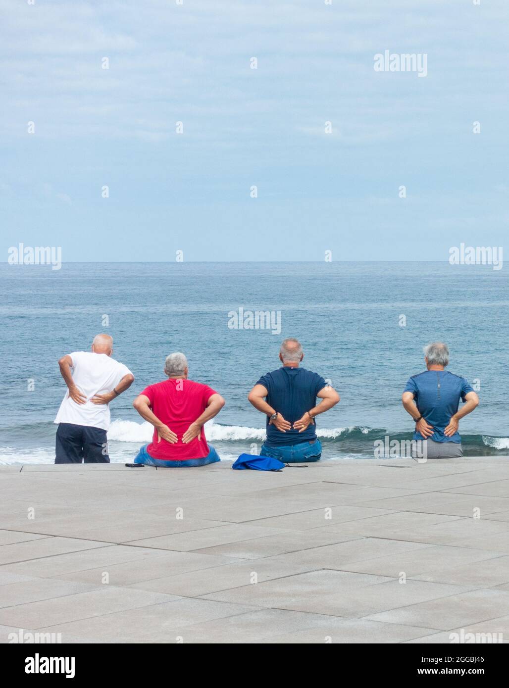 Rückansicht älterer Männer, die Übungen im unteren Rückenbereich mit Blick auf das Meer machen. Stockfoto
