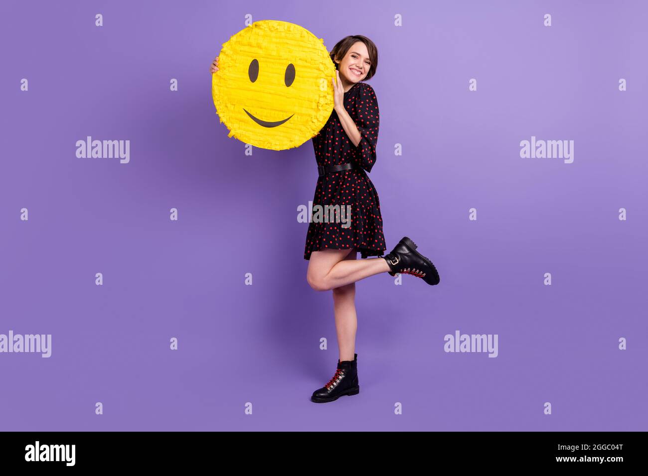 In voller Länge Körpergröße Ansicht der attraktiven fröhlichen Mädchen hält umarmenden gelben Smiley posiert isoliert über hellen violett lila Farbe Hintergrund Stockfoto
