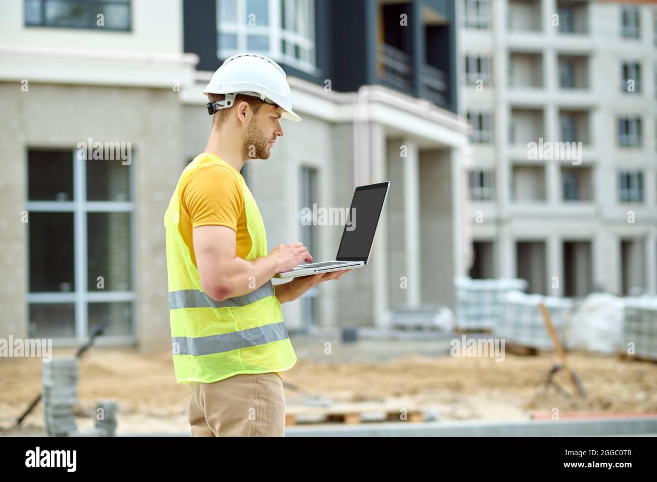Ernsthafter Mann in schützender Kopfbedeckung, der an seinem Laptop arbeitet Stockfoto