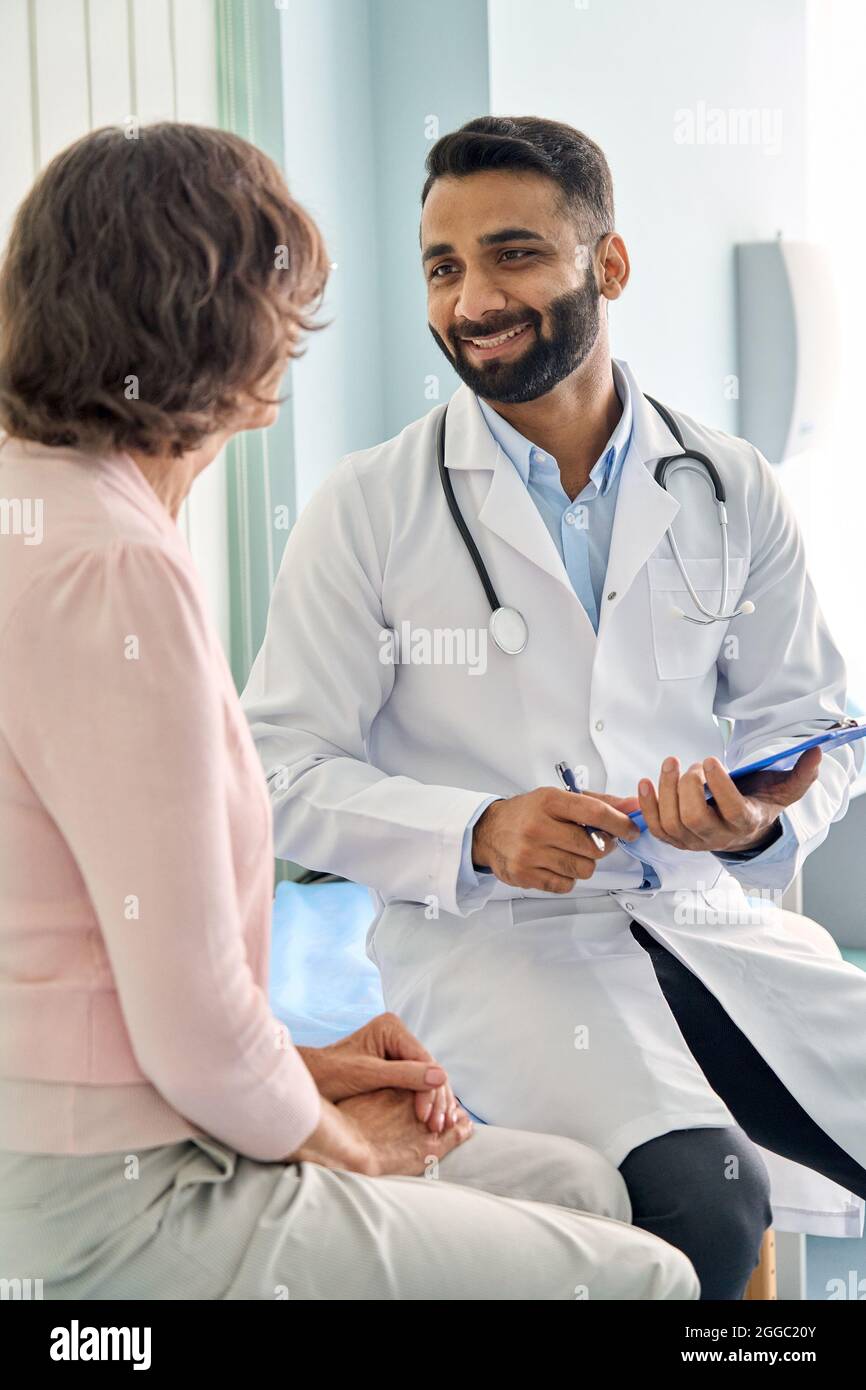 Glücklicher indischer Arzt, der weibliche ältere Patientin im Krankenhaus konsultiert. Vertikal. Stockfoto Glücklicher indischer Arzt, der weibliche ältere Patientin im Krankenhaus konsultiert. Vertikal. Stockfoto