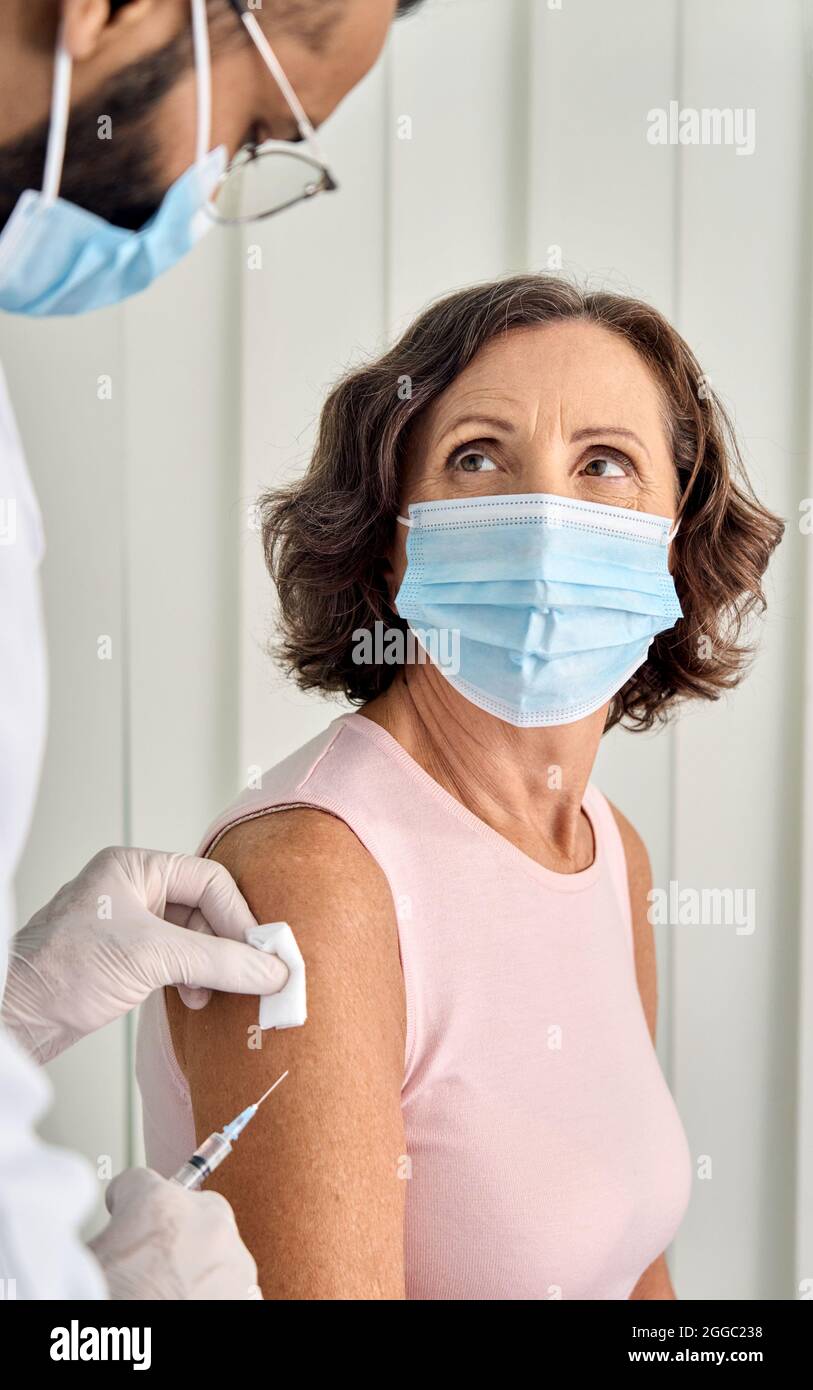 Ältere Dame mit Gesichtsmast, die in der Klinik eine Impfinjektion bekommt. Vertikal. Stockfoto