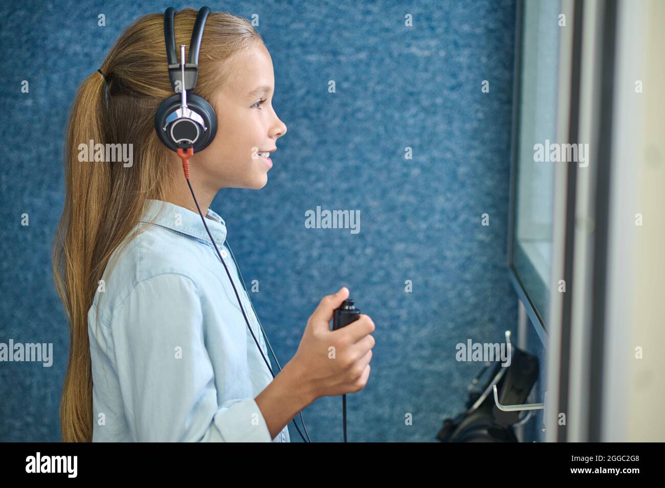 Lächelndes Mädchen in Kopfhörern im audiometrischen Raum Stockfoto