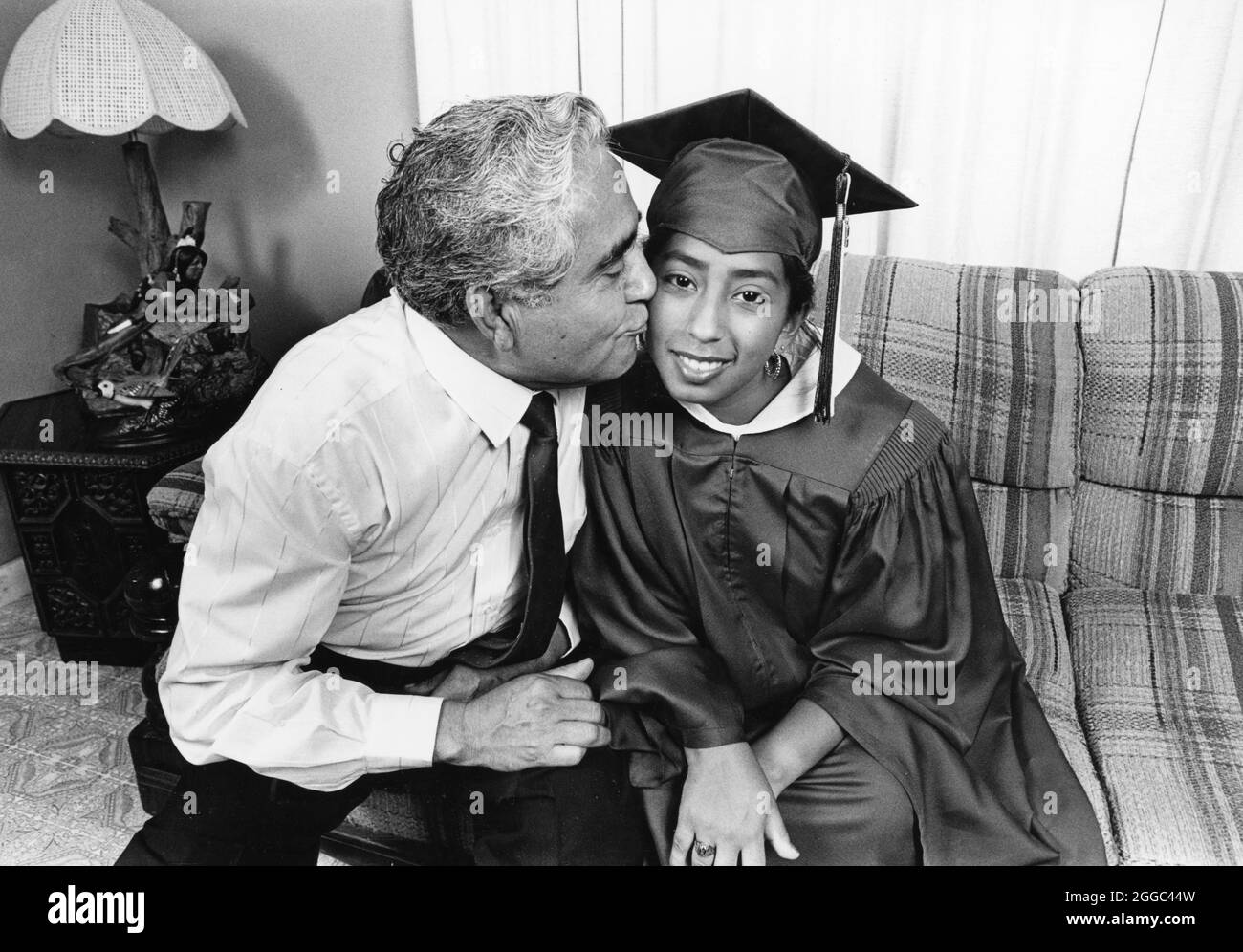 San Antonio Texas USA, um 1990: Weibliche High School Senior mit Mütze und Kleid wird von ihrem Vater zu Hause vor ihrer Eröffnungszeremonie von der Edgewood High School küsst. Ihr Vater, Demetrio Rodriguez, ist der genannte Kläger im unabhängigen Schulbezirk Rodriguez gegen San Antonio, Dies führte zu der bahnbrechenden Klage von Edgewood gegen Kirby, die den Staat Texas zwang, seine Finanzierung öffentlicher Schulen zwischen Bezirken, die reichen und weißen Schülern dienen, und denen, die armen und Minderheitsstudenten dienen, gerechter zu gestalten. MR es-0122 Model veröffentlicht ©Bob Daemmrich Stockfoto