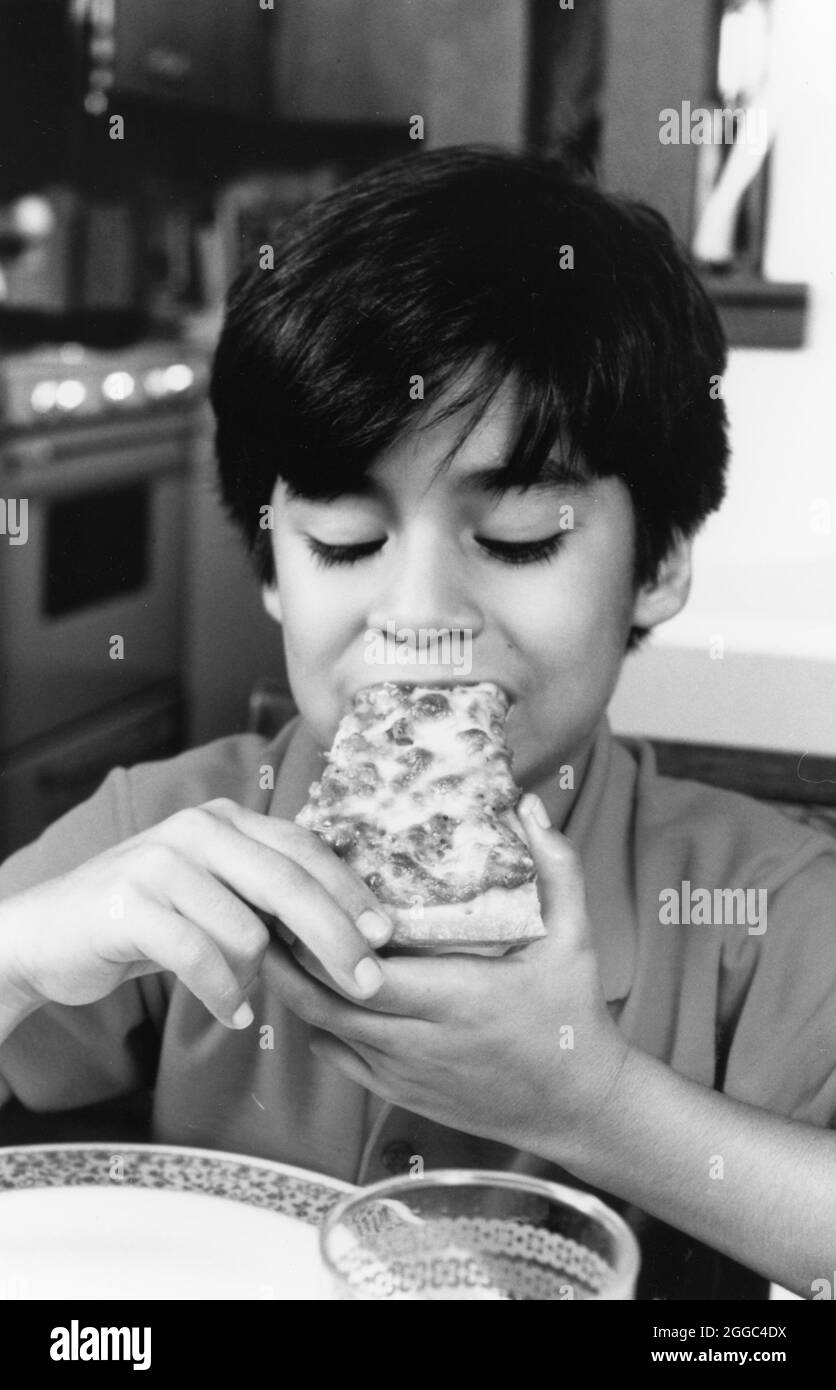 Austin Texas USA, um 1988: Hispanic Boy isst Pizza zu Hause. Keine Ausweise (Original in Farbe) ©Bob Daemmrich Stockfoto