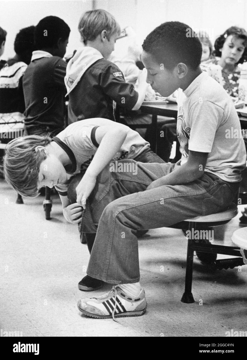 Austin Texas USA, 1984: Patrick Skeaton, der sein rechtes Bein wegen Spina bifida verlor, interagiert mit einem neugierigen Klassenkameraden in der Schulcafeteria der Wooten Elementary. Später wurde er mit einer Beinprothese ausgestattet. Teil einer erweiterten Fotofunktion. ©Bob Daemmrich Stockfoto