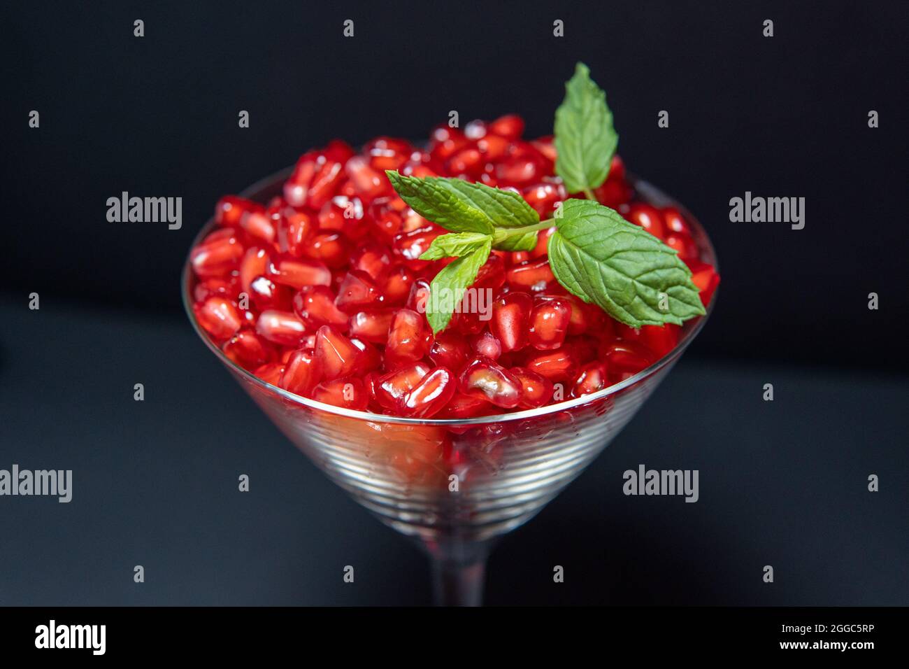 Gesunde Granatapfelkerne in Cocktailglas mit Minze auf dunklem Grund Stockfoto