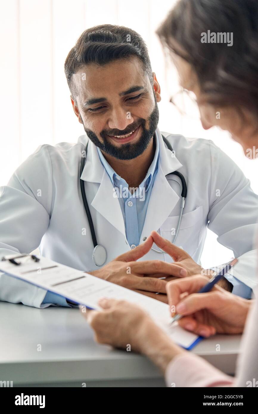 Lächelnde indische Ärztin, die weibliche Patientin im Klinikkrankenhaus konsultiert. Vertikal. Stockfoto