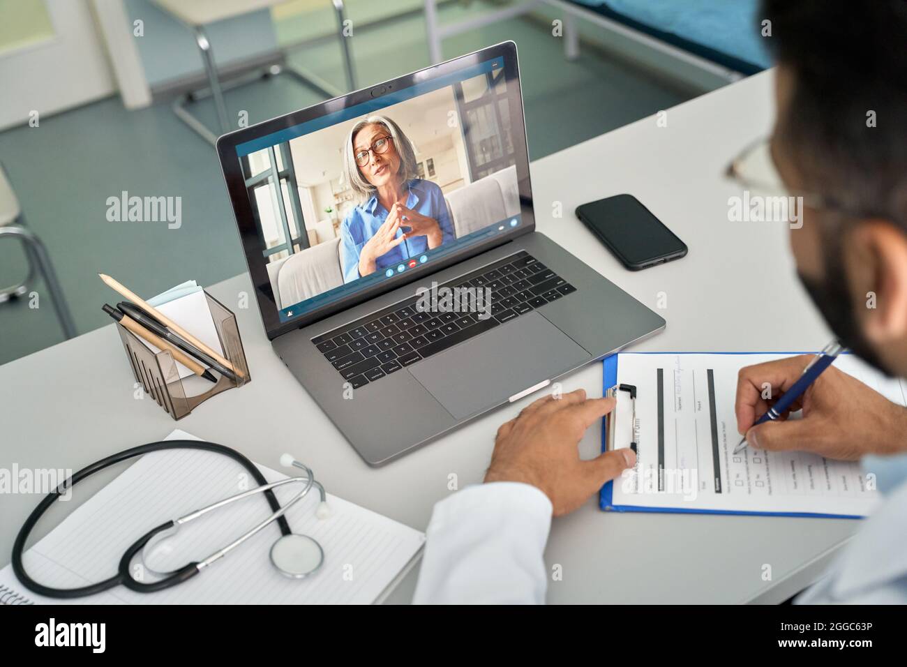 Indischer männlicher Arzt in der Klinik, der weibliche Patientin mit einem Laptop-Computer konsultiert. Stockfoto