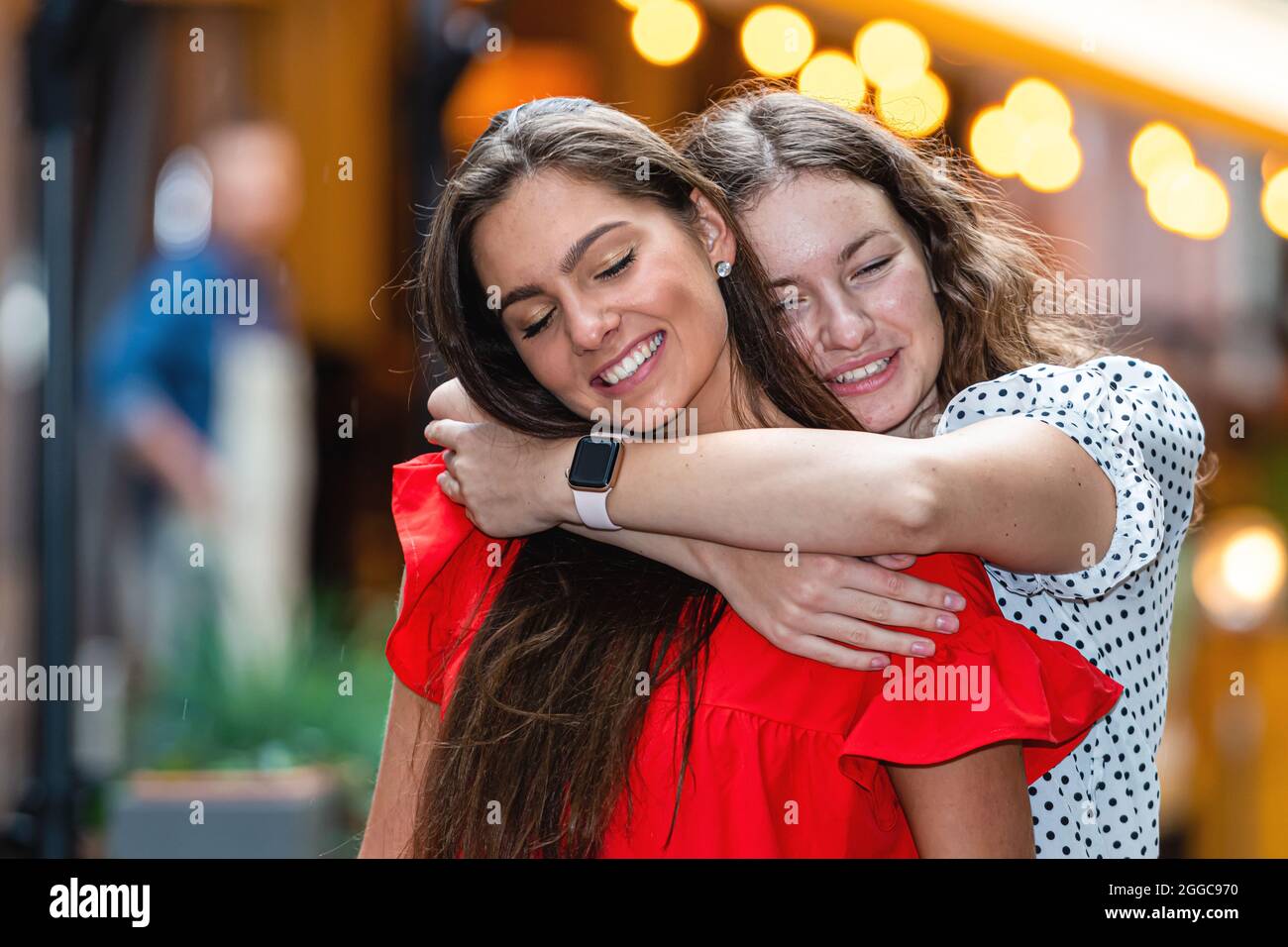 Zwei positive Freundinnen, die Spaß haben, lachen, umarmen und verrückt werden, Bokeh Lichter Hintergrund Stockfoto