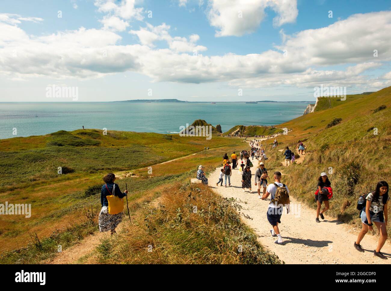 Menschen, die den Fußweg hinunter zur Durdle Door gehen, der ikonischsten Landschaft der Jurassic Coast mit ihrem natürlichen Kalksteinbogen. Dorset, Großbritannien. August 2021 Stockfoto