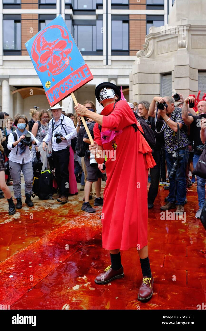 London, Großbritannien. Ein Protestler steht in einem Pool von gefälschtem Blut im Aussterben Rebellions 'Blutgeld'-marsch, der die städtischen Institutionen anpicht. Stockfoto