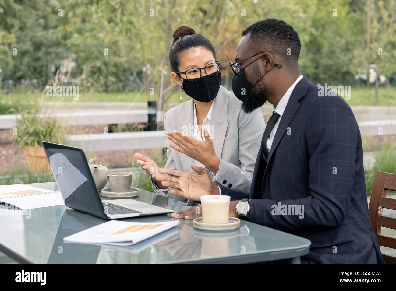 Zwei selbstbewusste Angestellte in formalwear und Schutzmasken diskutieren im Outdoor Cafe über neues Geschäftsprojekt Stockfoto