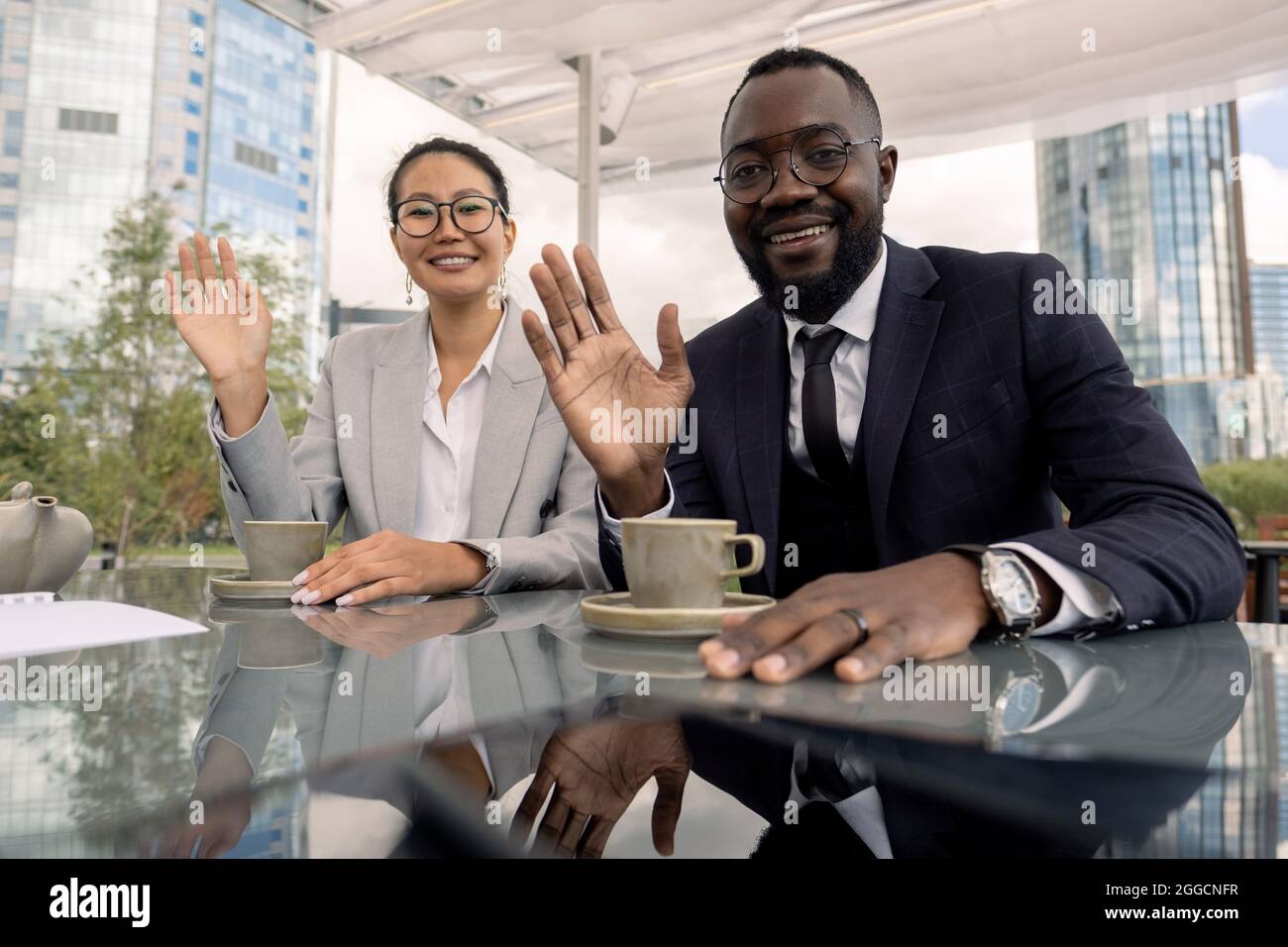 Asiatische und afrikanische Büroangestellte winken ihren Kollegen während eines Online-Meetings vor dem Laptop im Café im Freien die Hände Stockfoto