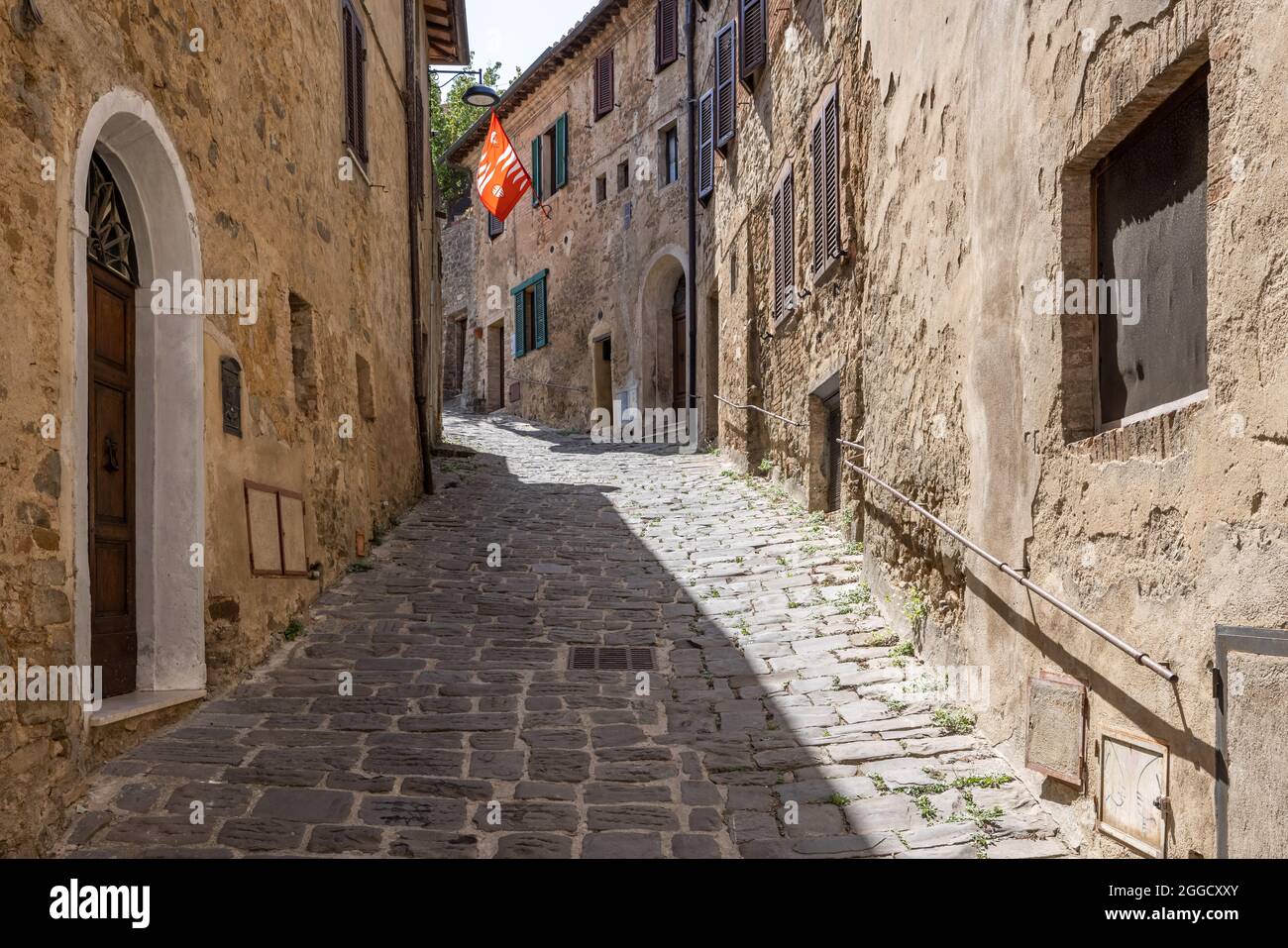 Eine schmale mittelalterliche gepflasterte Straße mit einer roten Flagge in der tuskanischen Stadt Montalcino Stockfoto