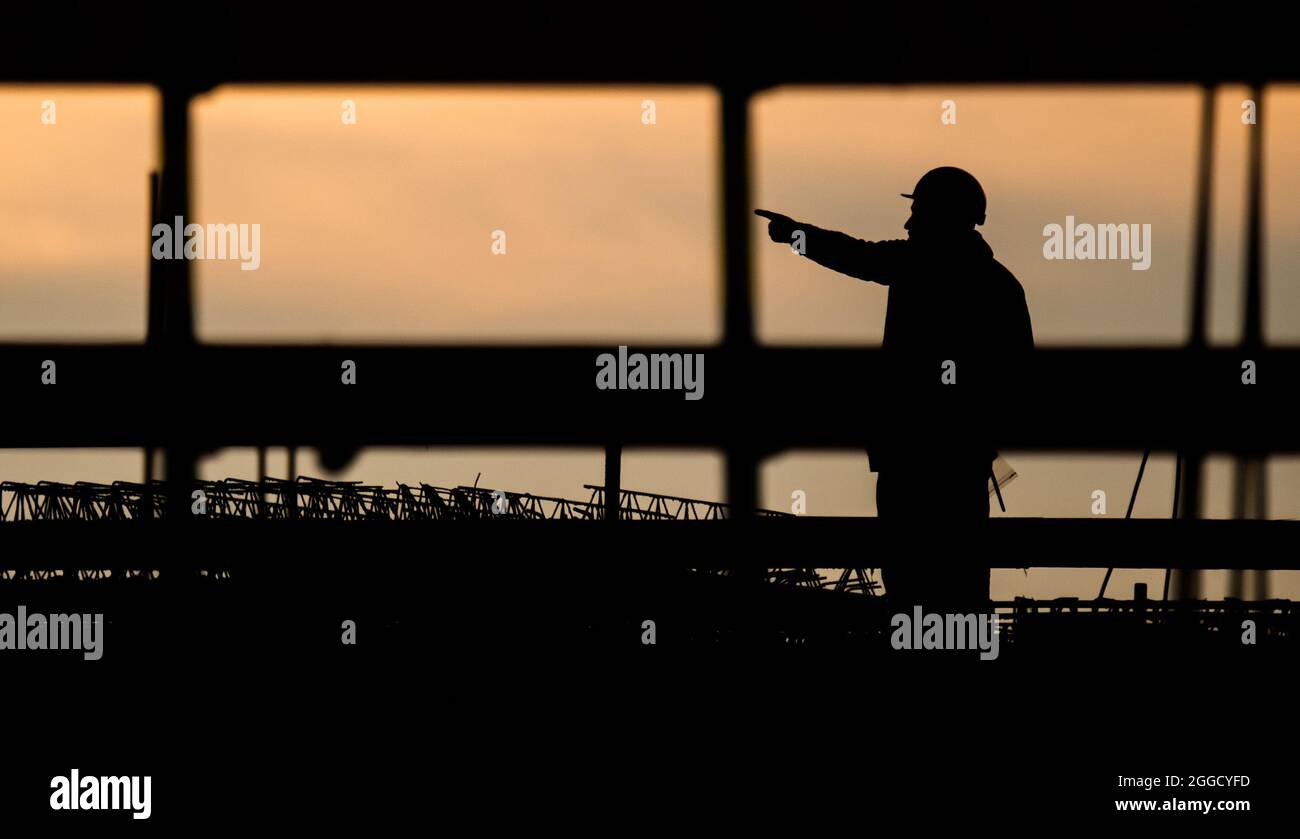 Hannover, Deutschland. August 2021. Die Silhouette eines Bauarbeiters hebt sich vom verfärbten Morgenhimmel auf einer Baustelle ab. Die Bundesagentur für Arbeit gibt die Arbeitsmarktstatistik für den Monat August 2021 bekannt. Quelle: Julian Stratenschulte/dpa/Alamy Live News Stockfoto