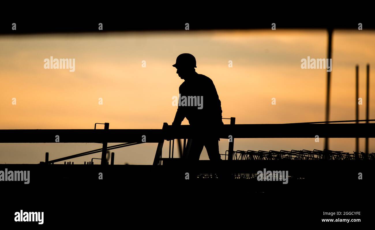 Hannover, Deutschland. August 2021. Die Silhouette eines Bauarbeiters hebt sich vom verfärbten Morgenhimmel auf einer Baustelle ab. Die Bundesagentur für Arbeit gibt die Arbeitsmarktstatistik für den Monat August 2021 bekannt. Quelle: Julian Stratenschulte/dpa/Alamy Live News Stockfoto