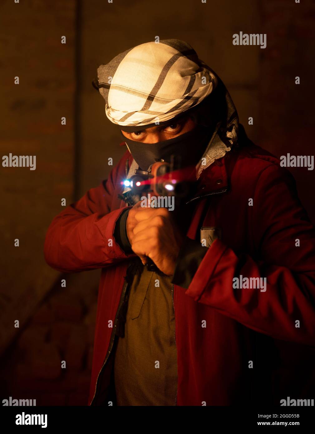 Terrorist oder Gangster mit Gesichtsschutz, der die Waffe an einem verlassenen Ort auf die Kamera zeigt. Stockfoto