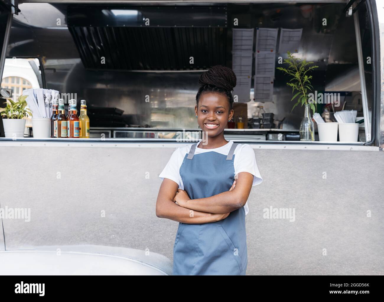 Porträt einer Unternehmerin, die an einem Food-Truck steht. Inhaber eines kleinen Unternehmens, der eine Schürze trägt und die Kamera im Freien ansieht. Stockfoto
