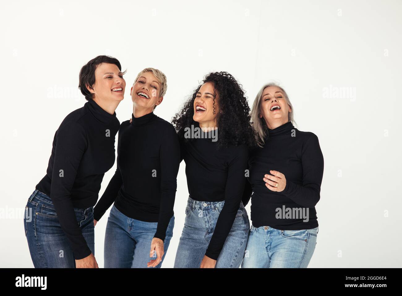 Fröhliche Gruppe von verschiedenen Frauen, die ihr Leben in einem Studio feiern. Vier körperpositive Frauen unterschiedlichen Alters lächeln fröhlich, während sie Jeans aga tragen Stockfoto