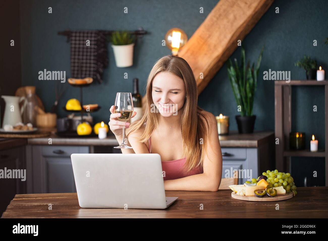 Glückliche junge Frau, die Weißwein trinkt, während sie im Wohnzimmer mit ihrem Freund chattet Stockfoto