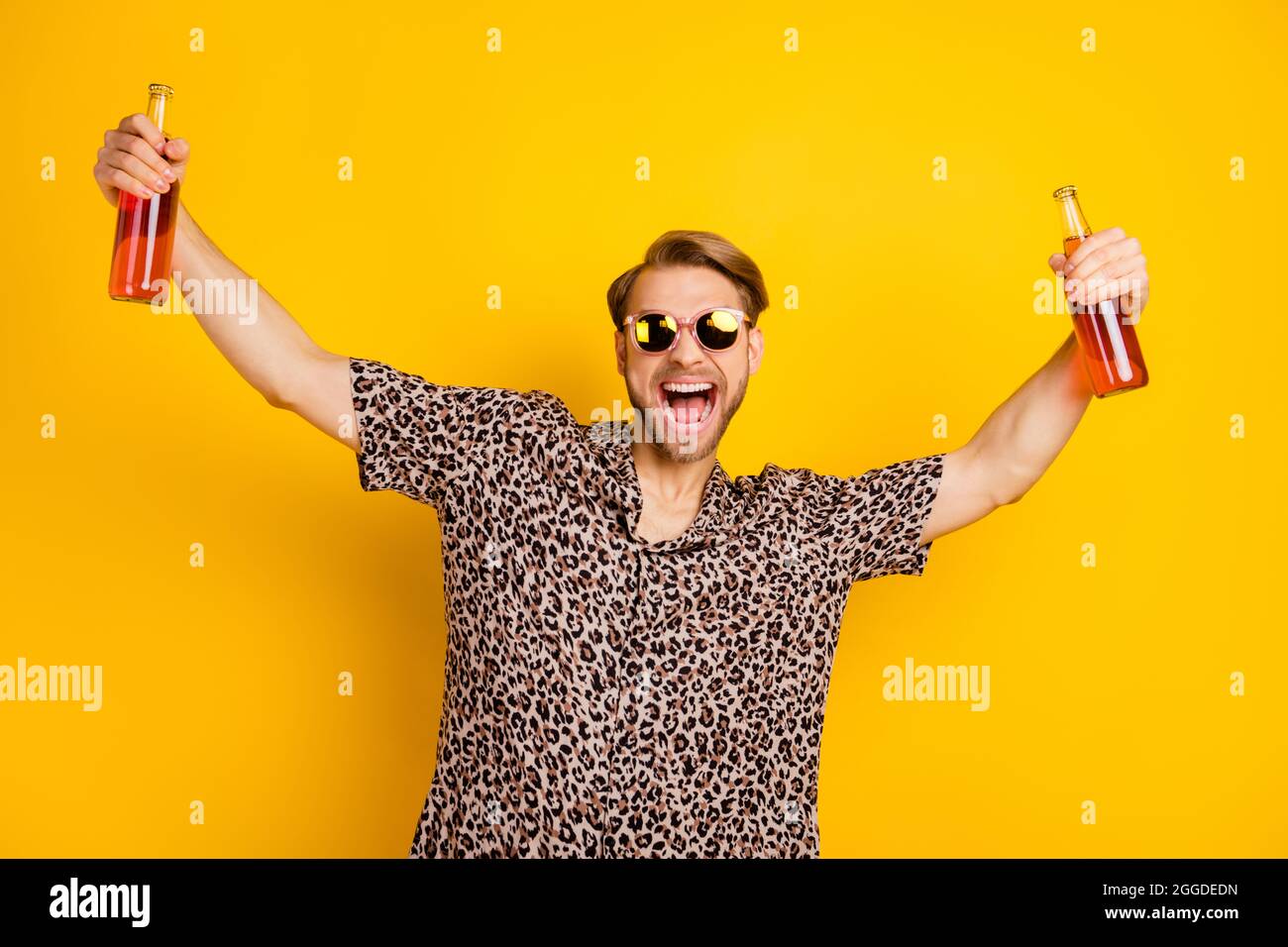 Foto von ziemlich charismatischen jungen Gentleman gekleidet drucken Hemd dunkle Gläser halten zwei Bierflaschen isoliert gelben Hintergrund Stockfoto