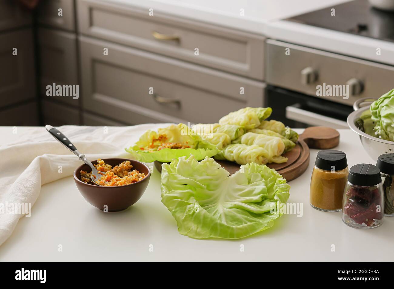 Holzbrett mit rohen gefüllten Kohlrollen und Zutaten auf dem Tisch in der Küche Stockfoto