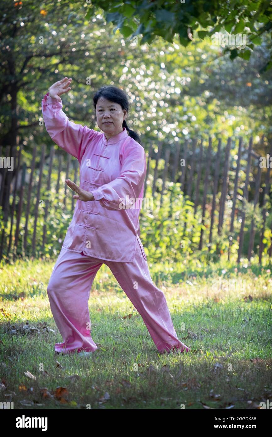 Eine attraktive Frau im rosa Seidenanzug Tai Chi trainiert anmutig in einem Park in Queens, New York City. Stockfoto