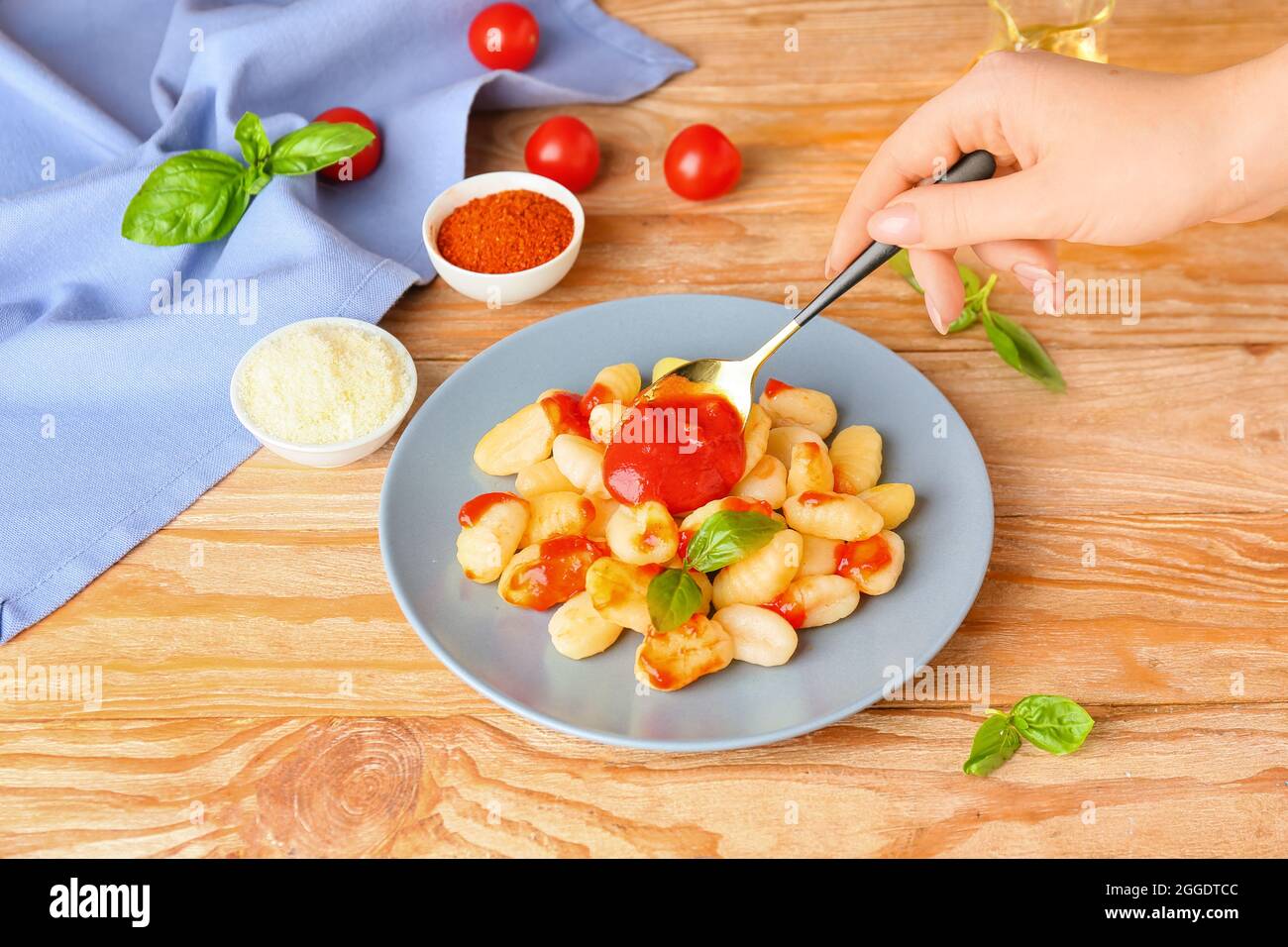Frau, die Tomatensauce auf den Teller mit leckeren Gnocchi auf dem Holztisch zugegeben hat Stockfoto