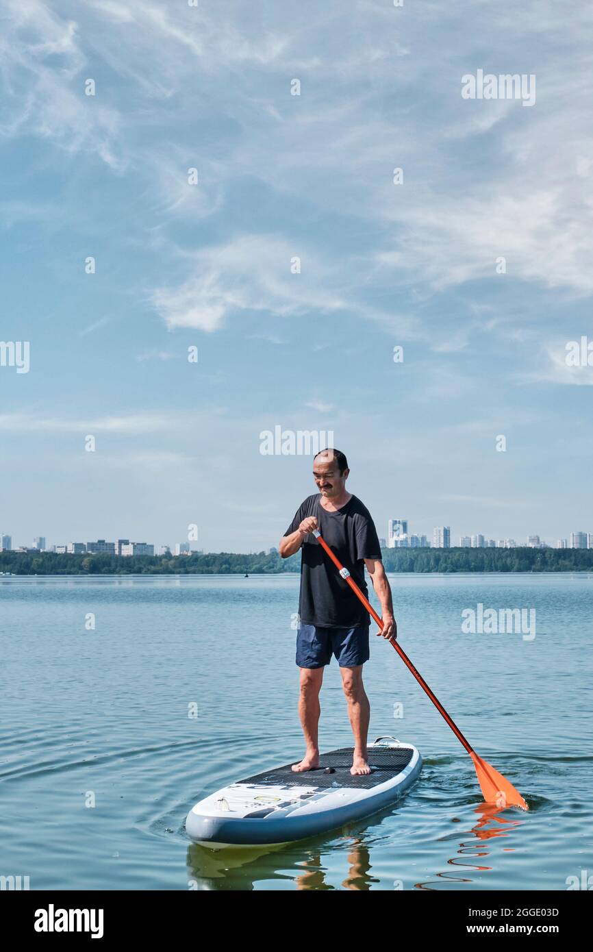 Asiatische ältere Mann auf supboard auf ruhigen See. Stockfoto