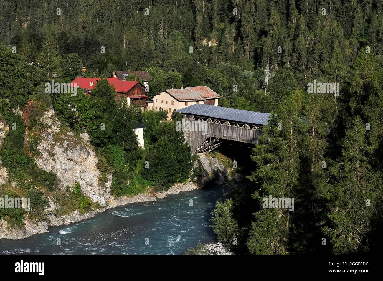 Diese robuste, 1878 erbaute, überdachte Holzbrücke hat eine Spannweite von 151 m über den Inn oder en, während sie durch eine felsige Schlucht bei Scuol in Graubünden oder Graubünden, Ostschweiz, überflusst. Scuol ist ein historischer Kurort im Unterengadiner Tal mit vielen renovierten traditionellen Häusern. Fast die Hälfte der Einwohner spricht Rätoromanisch, eine Nachkommenssprache des alten römischen Reiches, mit Deutsch zweiten und Italienisch dritten. In Rätoromanisch heißt die Brücke Punt d’en Scuol-Sot. Stockfoto
