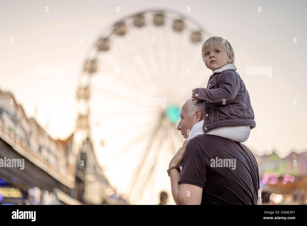 Glücklicher Vater mit seinem kleinen huckepack Sohn in einem Vergnügungspark Stockfoto