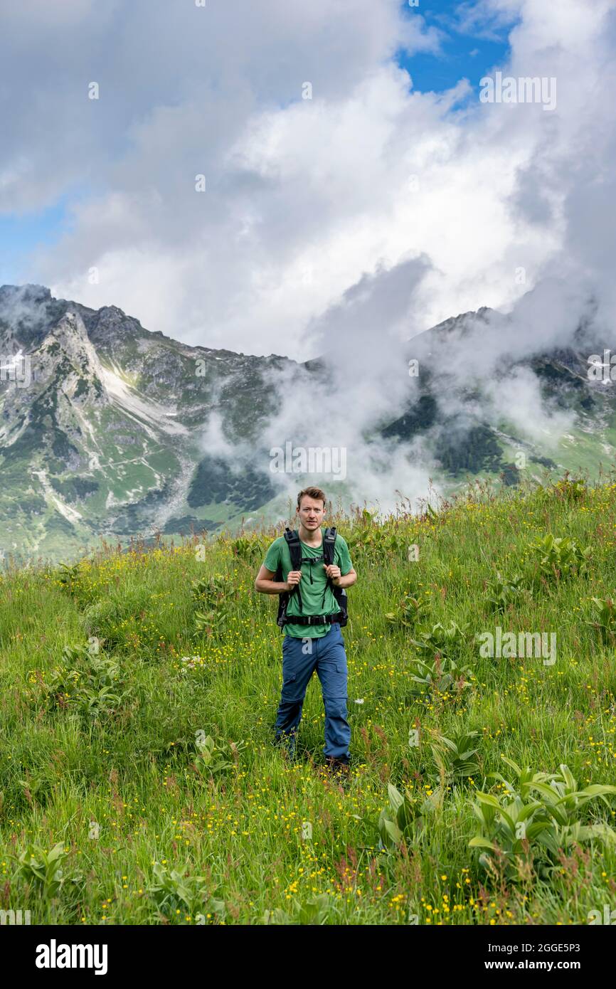 Junger Mann, Wanderer auf einer Wiese, Berggipfel dahinter, Abstieg von der Rappenseehütte, Allgäuer Alpen, Allgäu, Bayern Stockfoto