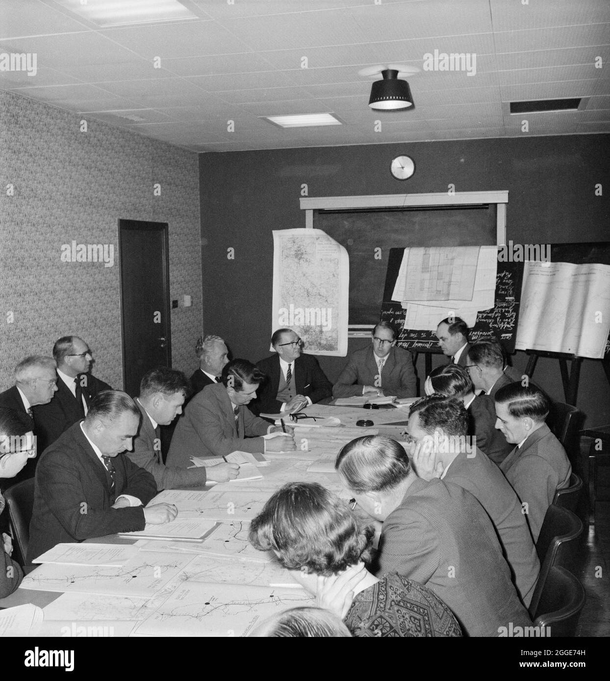 Eine Gruppe von Leuten im Mill Hill Büro von John Laing &amp; Son Ltd, die ein Treffen über die Autobahn Birmingham nach Preston (M6) mit Dokumenten und Plänen der Autobahn über den Tisch verteilt haben. Dieses Bild wurde als Teil des Breaking New Ground Project in Zusammenarbeit mit dem John Laing Charitable Trust in den Jahren 2019-20 katalogisiert. Stockfoto