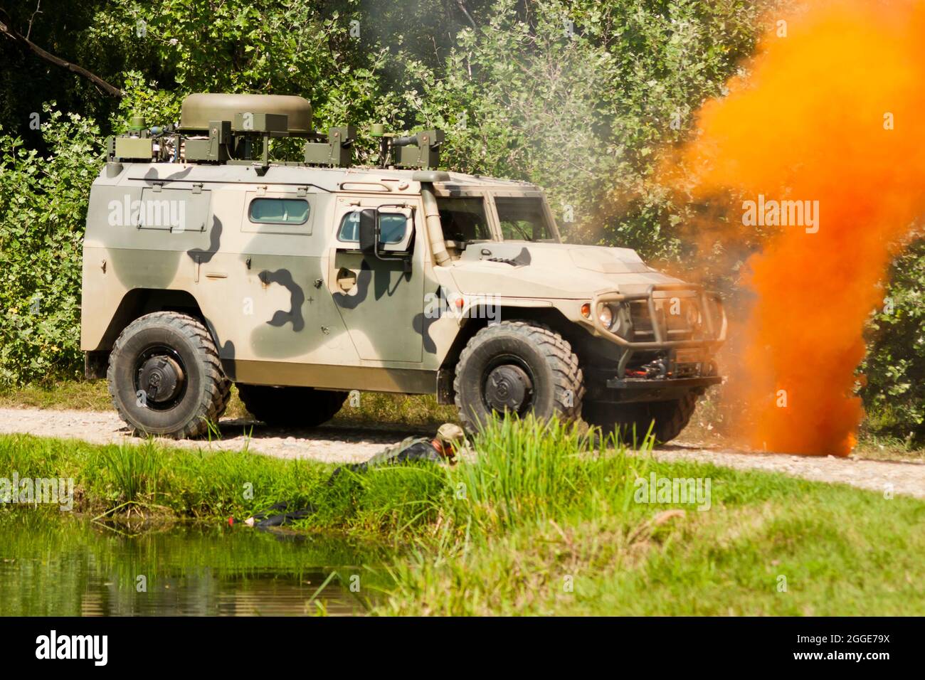 Fragment einer militärischen Demonstrationsvorstellung. Ein militärisch gepanzertes Fahrzeug steht auf einer unbefestigten Straße neben einer Signal-Rauchbombe Stockfoto