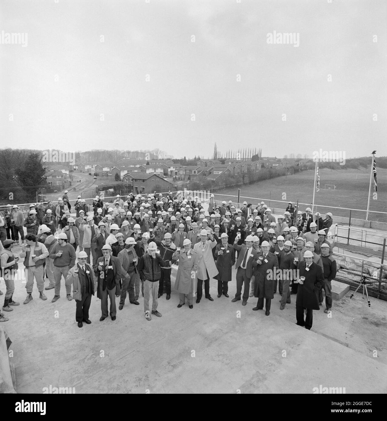 Projektverantwortliche und eine große Gruppe von Mitarbeitern posieren mit Hartmützen auf dem Dach des neuen Forschungsgebäudes am Glaxo-Standort in Ware zum Richtfest. Laing baute zwischen 1985 und 1987 das neue Forschungsgebäude, das Pförtnerhaus und den Dienstleistungsblock am Standort Ware Glaxo, dieser &#xa3;7,5-m-Vertrag war Phase IV der Bauarbeiten am weitläufigen Gelände und mehrere Gebäude wurden in den folgenden Jahren hinzugefügt. Stockfoto