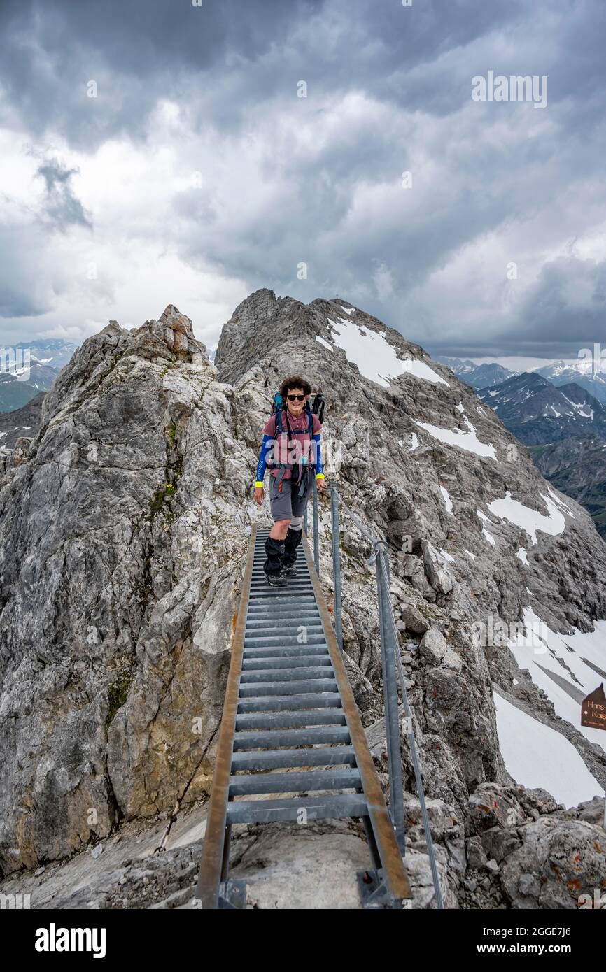 Wanderer auf einer Metallbrücke auf einem Felsen, Höhenweg mit Schneeresten, Bergpanorama mit hohem Licht, dramatischer Wolkenhimmel, Heilbronner Weg Stockfoto