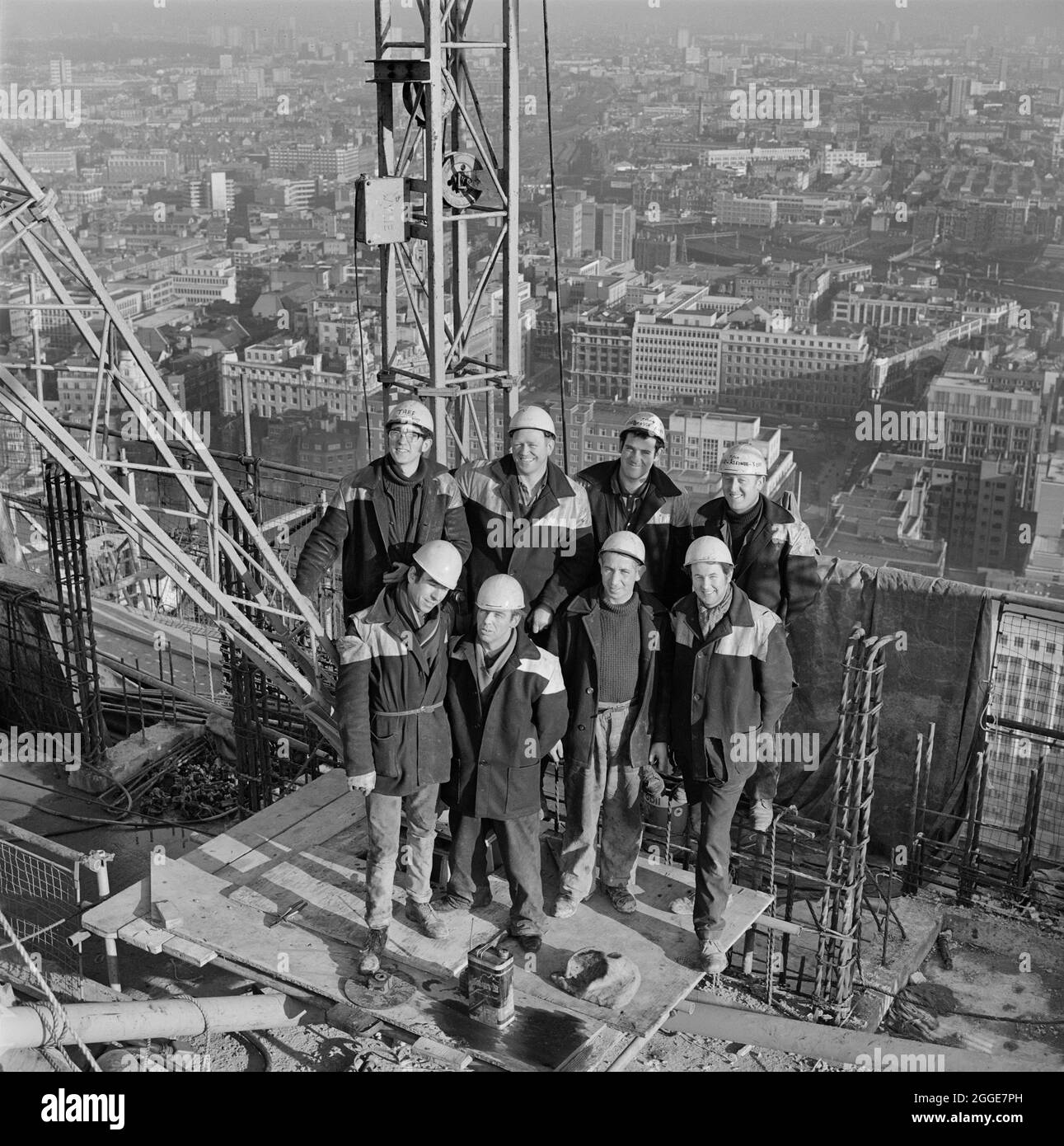 Das Team der Arbeiter von Laing, die an der Demontage eines Turmdrehkrans arbeiteten, posierte für ein Foto auf dem Dach eines Turms, möglicherweise des Cromwell Tower, auf der Baustelle in Barbican. Eine beschnittene Version dieses Bildes wurde in der März 1969 Ausgabe des Laing-Newsletters Team Spirit veröffentlicht. Sie nennt die Arbeiter von Laing wie folgt von links nach rechts: Hintere Reihe; J. Williams (Monteur), J. O'Keefe (Kranfahrer), J. Steeden (verantwortlich) und Ginger Weaving (Monteur). Vordere Reihe; S. O'Brian (Banksman), C. Moffat (Kranfahrer), M. Kelly (Gerüstbauer) und J. O'Shea (Gerüstbauer). Stockfoto